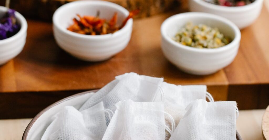 Close-up of herbal tea bags and bowls of dried herbs on a wooden table for brewing.