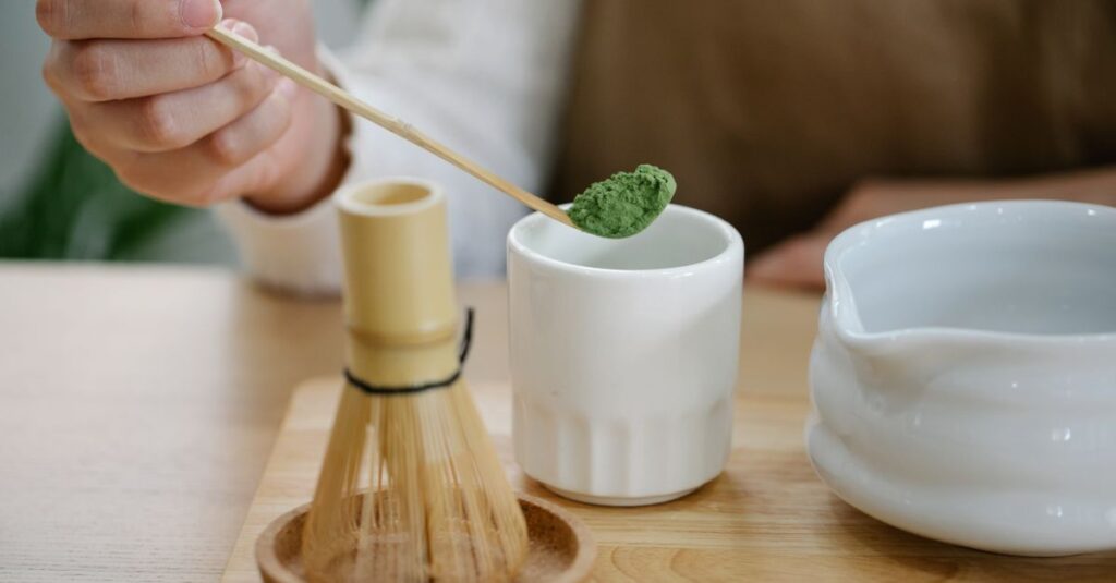 A person prepares matcha tea using traditional tools on a wooden table.