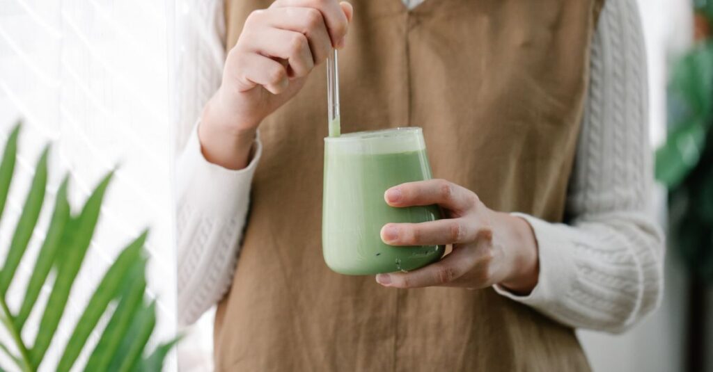 Close-up of a woman stirring a creamy matcha latte in a cozy indoor setting.