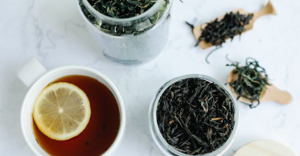 Close-up shot of a cup of tea with a lemon slice and jars of loose leaf tea on a marble surface.