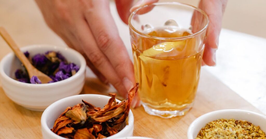 Person arranging herbal tea with various herbs on wooden board.