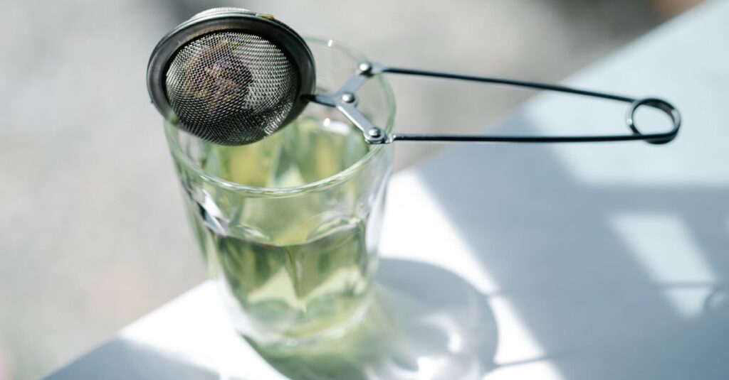 A tea strainer resting on a glass with sunlight casting shadows, creating a serene tea-making ambiance.