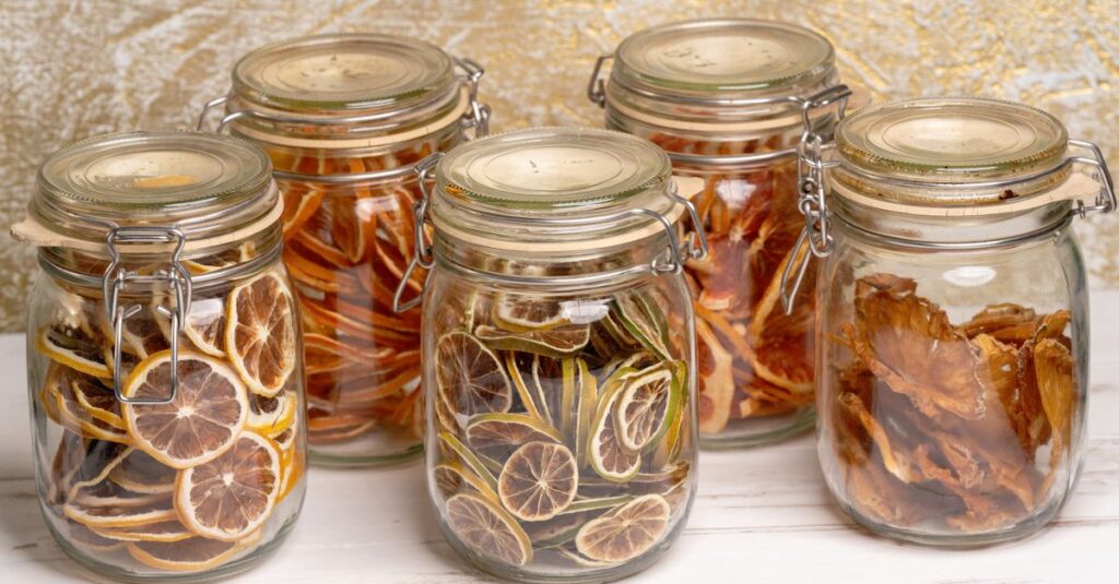 Colorful, preserved dried fruits arranged neatly in decorative glass jars on a white surface.