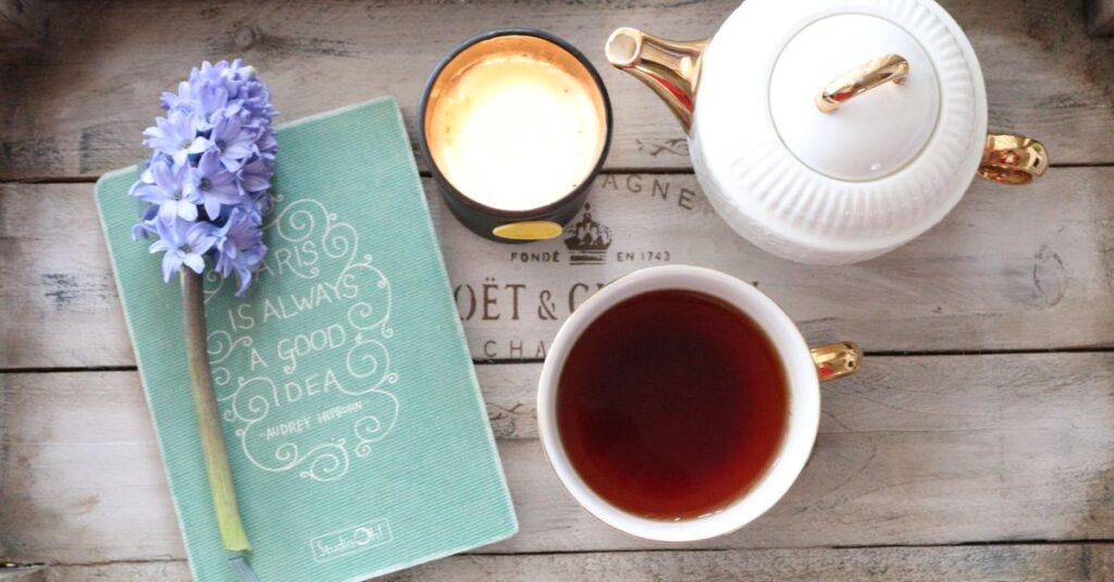 A cozy tea setup featuring a cup, teapot, notebook, and candle on a wooden tray.