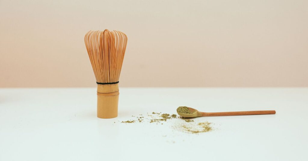 Elegant still life of a bamboo whisk and matcha powder on a spoon.