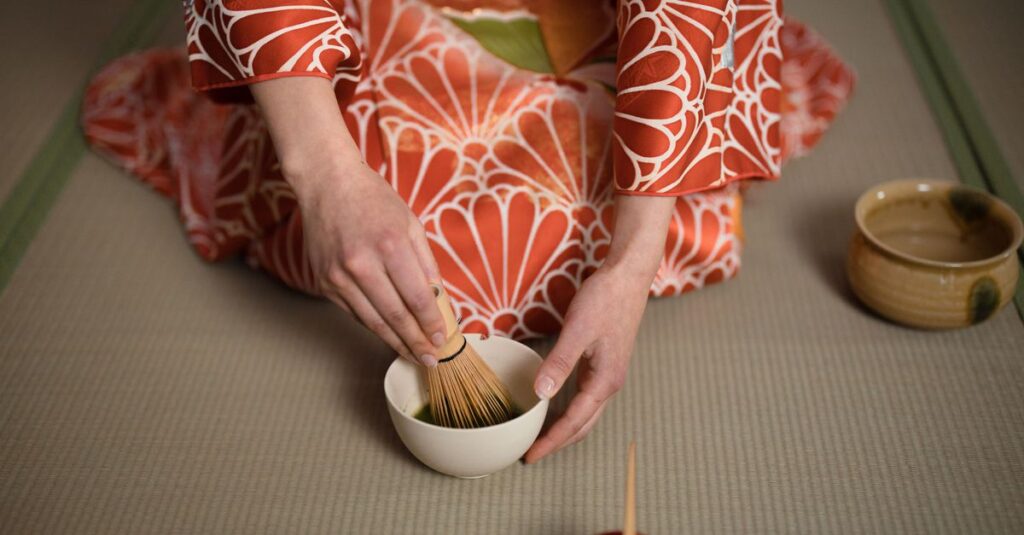 A person in a kimono preparing matcha tea in a traditional ceremony setting.