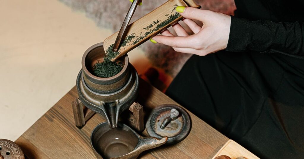 A person prepares tea by adding leaves with a bamboo scoop into a vintage teapot.