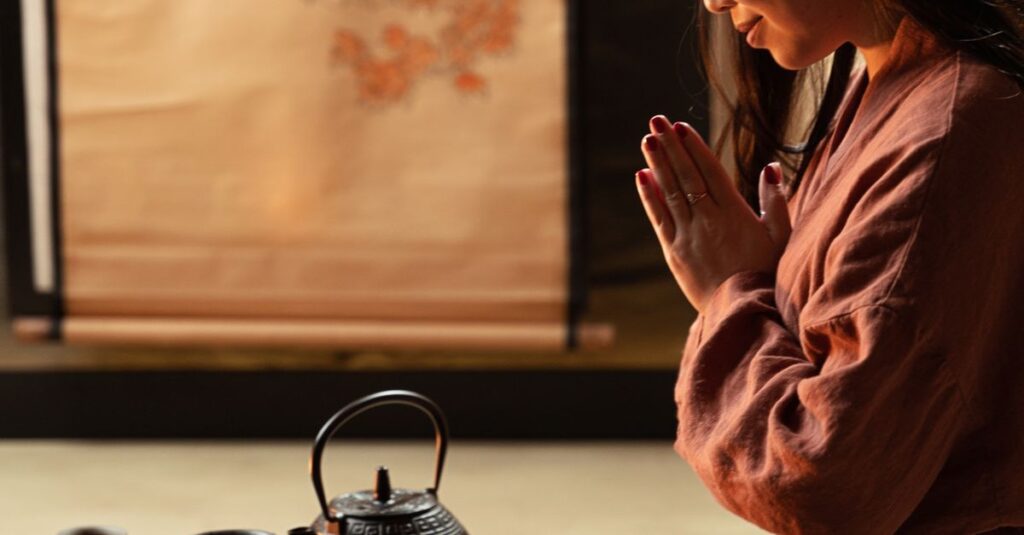 Asian woman performing a traditional tea ceremony indoors, kneeling in meditation.