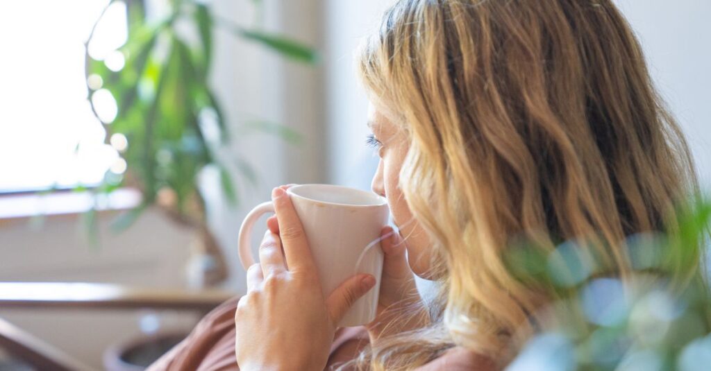 A blonde woman enjoys coffee indoors, creating a cozy and calming atmosphere.