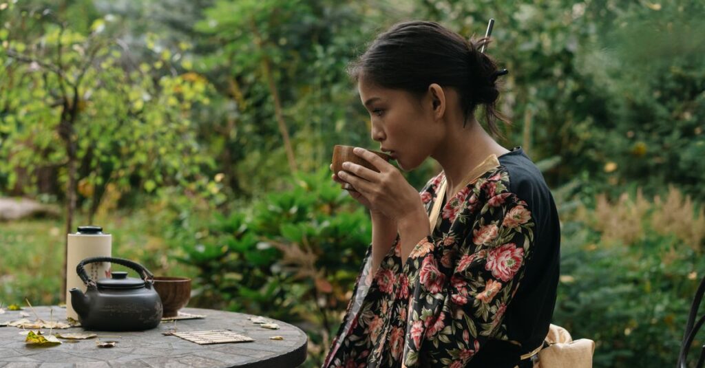Woman in kimono sipping tea outdoors at a rustic table. Calm and peaceful setting.