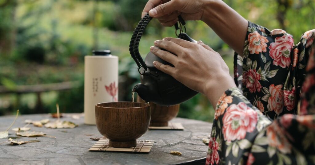 Hands pouring tea during a traditional Japanese tea ceremony in a peaceful garden setting.