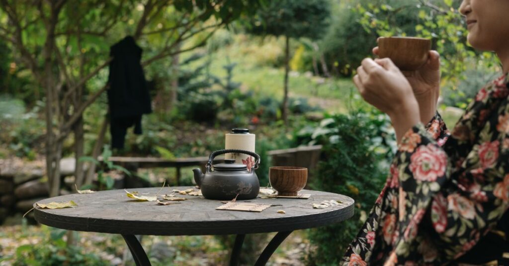 Asian woman in a kimono enjoys tea in a lush garden setting.