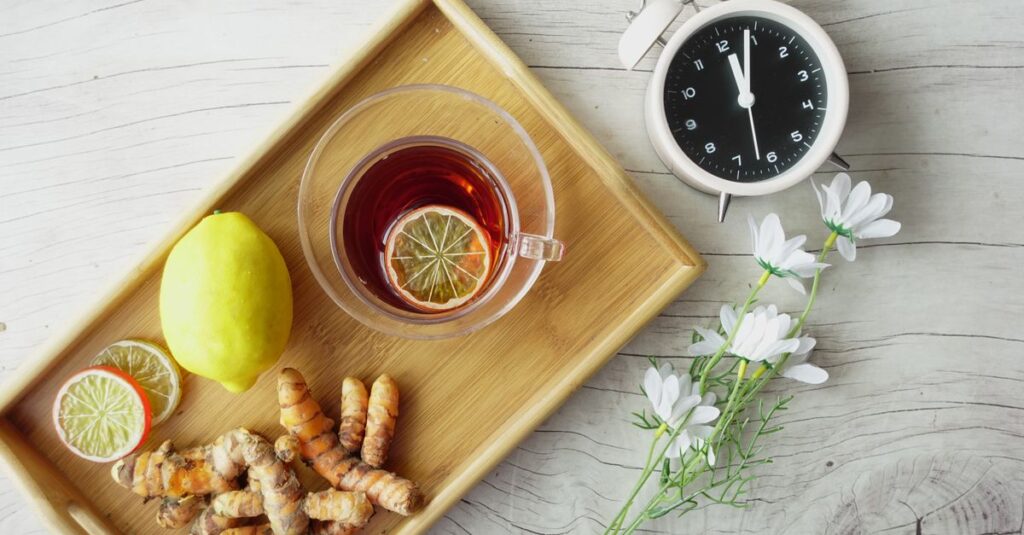 Overhead view of herbal tea with lemon, turmeric, and flowers on wooden tray. Healthy lifestyle concept.